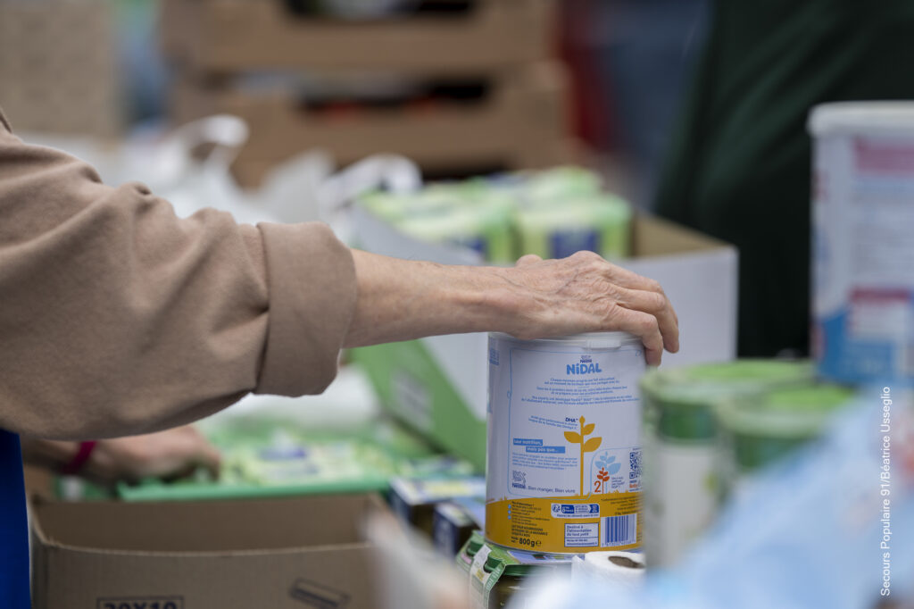 La main d'une bénévole du Secours populaire qui prend une boîte de conserve.